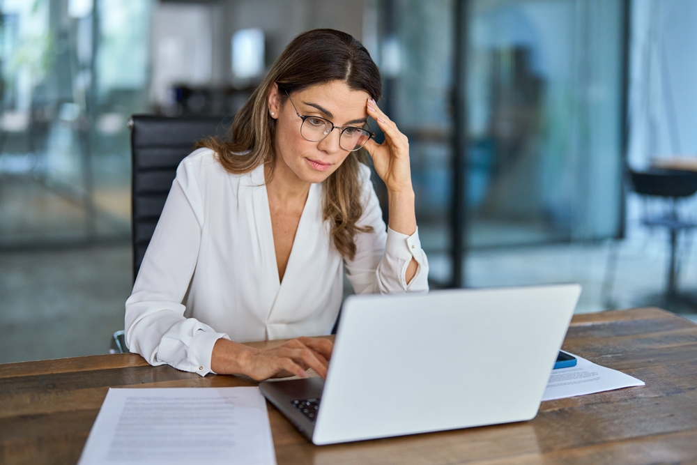 woman in an office setting looking at her laptop and appears to be frustrated
